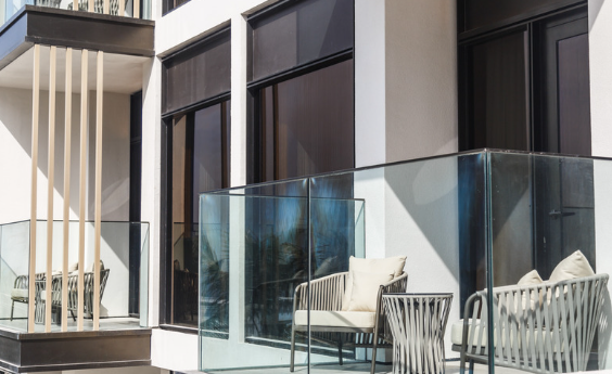Modern apartment balcony with glass railings and striped lounge chairs with cushions, beside large windows and sliding doors.