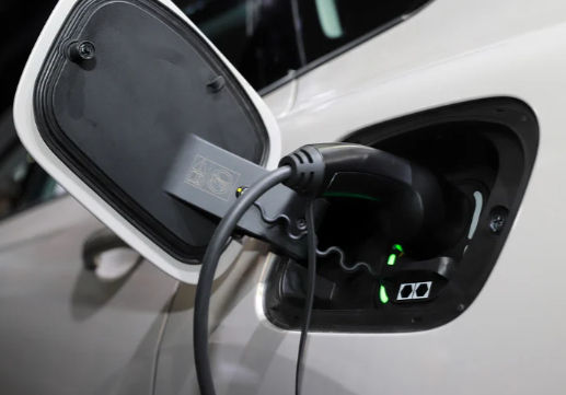 Electric car charging port with cable plugged in, green indicator lights glowing on a white vehicle.