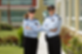 Two security guards in blue uniforms and caps stand confidently with arms crossed. They're outdoors, with a building in the blurred background.