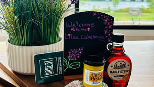 Gift basket with lavender, mustard, maple syrup and a Welcome to the Mac Lakehouse sign on a tray by a window.