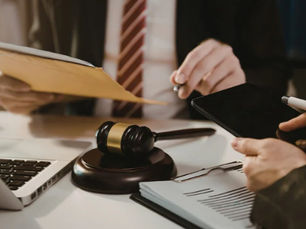 Lawyers review documents around a gavel on a desk, with a laptop and tablet in a formal office setting.