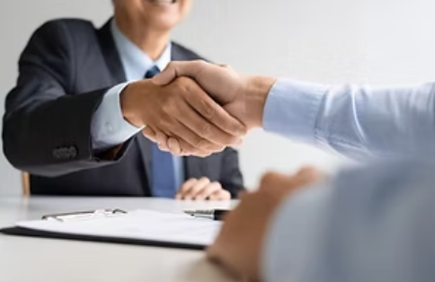 Business handshake between two people at a desk in a bright office, suggesting a deal or agreement.