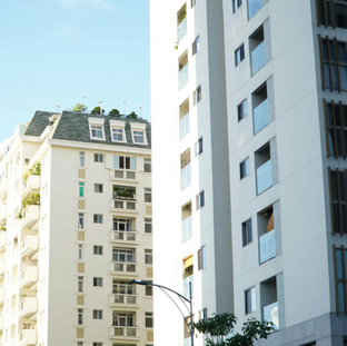 Sunlit apartment buildings against a blue sky, with a cream building on the left and a white modern tower on the right.