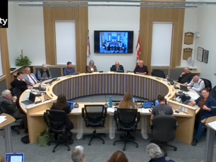 County council meeting with people seated around a circular table, large screen showing meeting image, Canadian flags, and "TheCounty" logo.