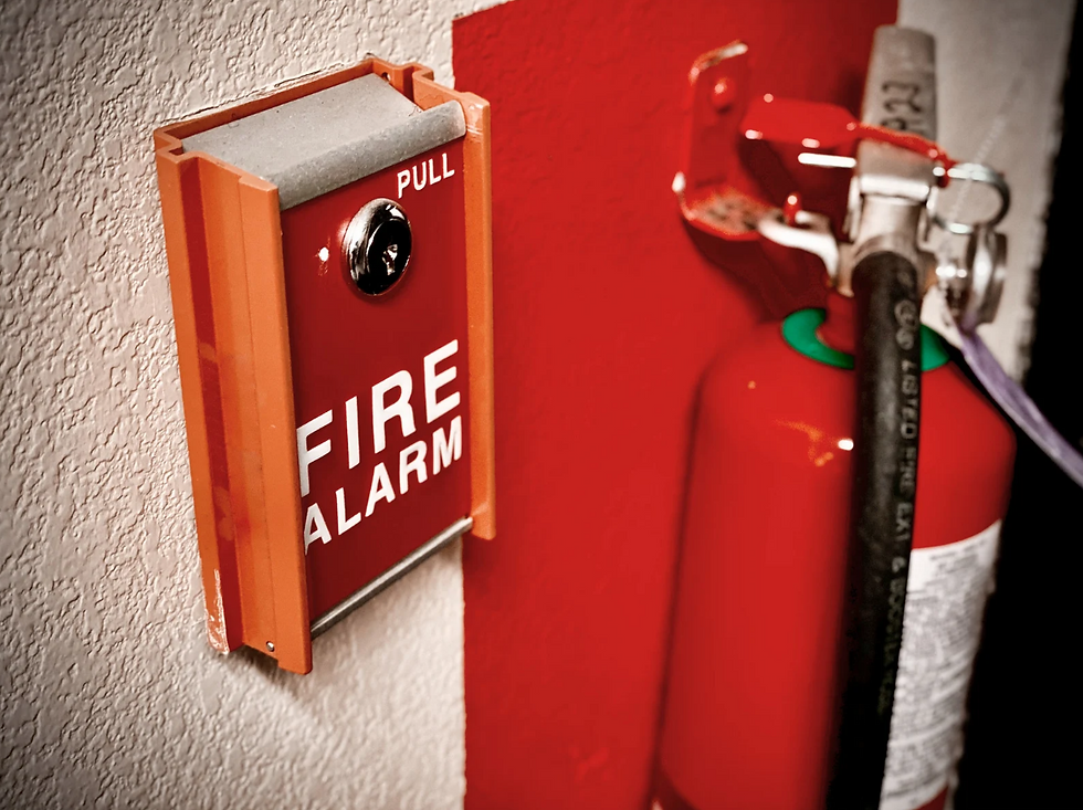 Red fire alarm pull station beside a red fire extinguisher on a wall, with PULL and FIRE ALARM text visible.