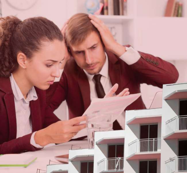 Worried office workers in maroon suits study papers beside a modern apartment model in a bright office.