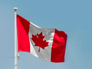 Canadian flag waving on a pole against a clear blue sky. The flag features a red maple leaf centered on white with red borders.