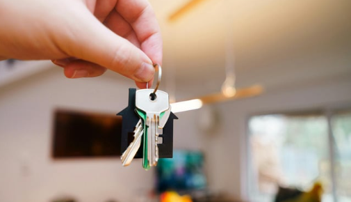 Hand holding a keyring with several keys in a softly blurred living room, warm and homey.