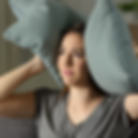 A woman covers her ears with a pillow because of the noise.