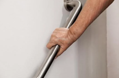 A hand grips a stainless steel support bar on a white wall, suggesting stability and support. The mood is secure and reassuring.