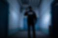 Security guard holding flashlight, stands in dimly lit hallway. "SECURITY" visible on jacket. Blue walls create an eerie atmosphere.