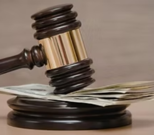 Judge’s gavel pressing on a stack of cash on a beige surface, symbolizing legal or financial pressure.