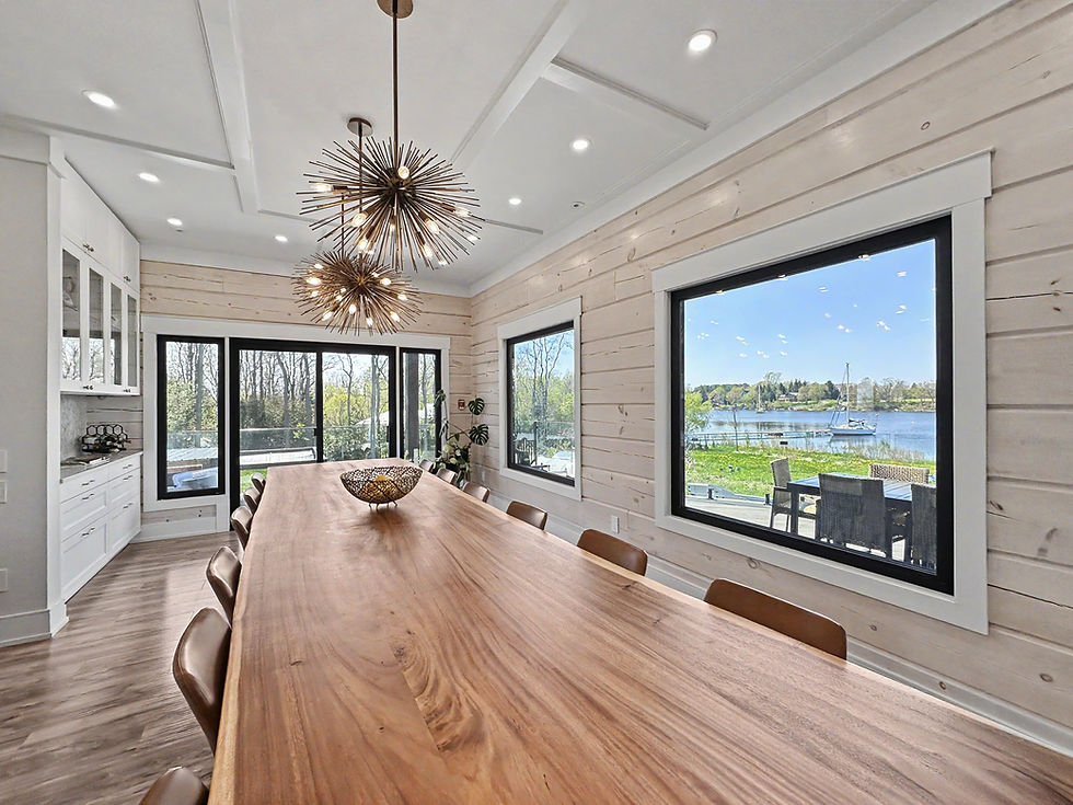 Modern dining room with long wooden table, starburst pendant lights, and large windows overlooking a lake and sailboats.