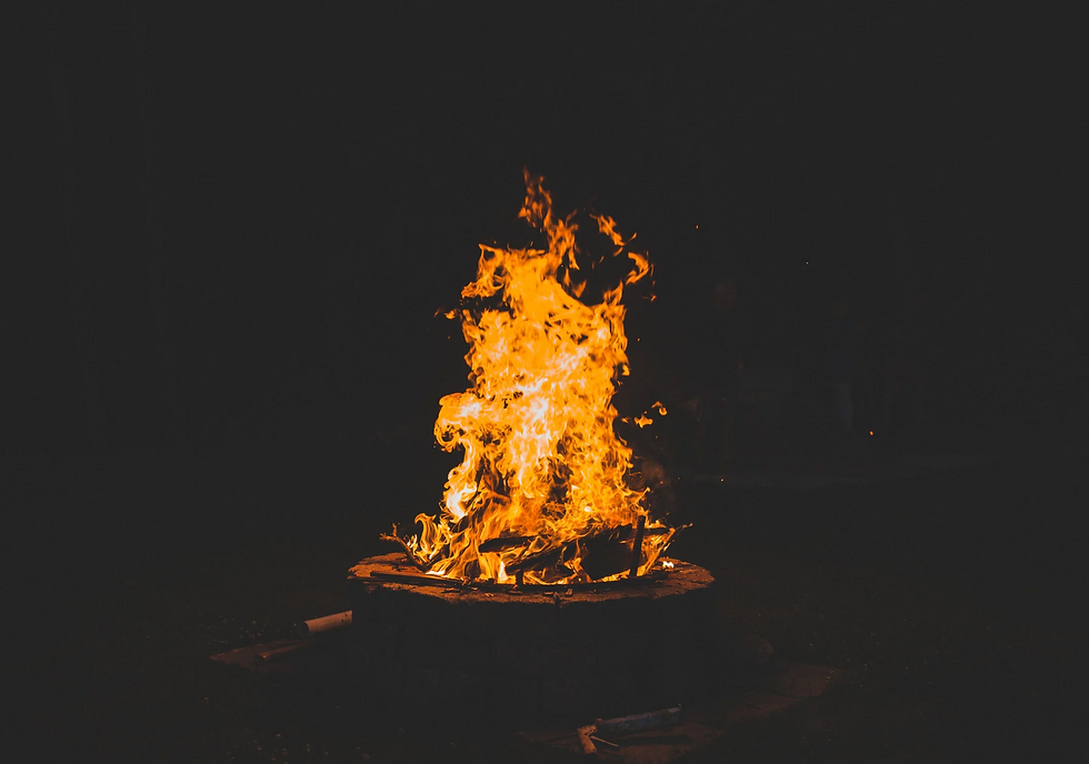 Bright orange campfire blazing in a stone fire pit at night against a dark background.