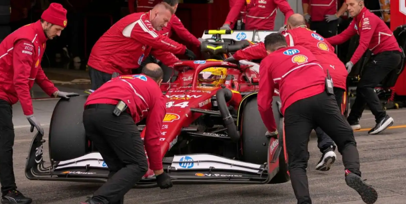 Ferrari mechanics push a Formula 1 car out of the garage with the driver inside. 