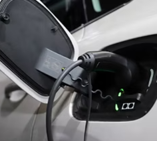 White electric car charging, plug inserted in the port with green indicator lights on a gray body.