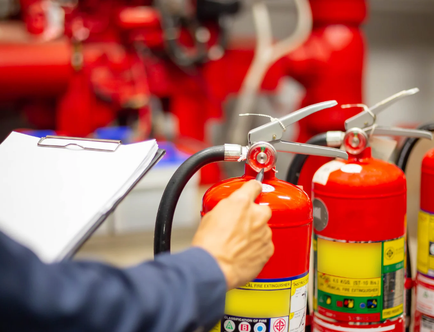 Person checks red fire extinguishers with a clipboard in a workshop, focused on safety inspection.