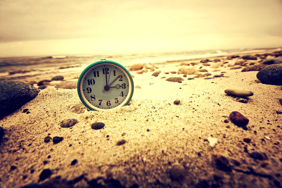 A traditional desk clock in a green frame, resting on a sandy beach