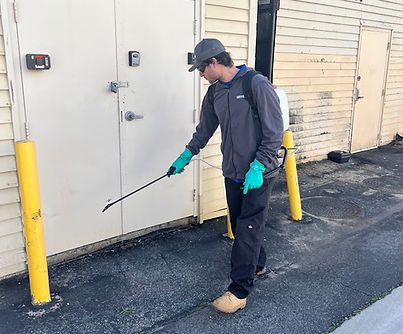 Pest control technician treating the exterior of a commercial building by spraying the doorway