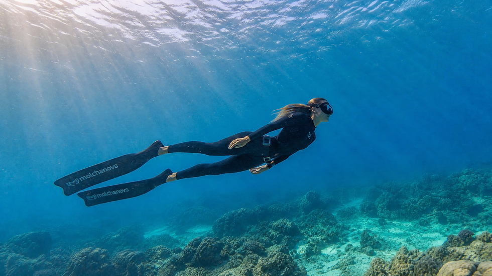 Freediver swimming horizontally above a coral reef in clear tropical blue ocean water with sunlight rays — reading underwater currents before diving, Plunge Waterwear dive skins dive suit UPF 50+