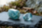 Rough natural aquamarine crystal next to a polished faceted aquamarine gemstone on slate — natural vs treated gemstones comparison