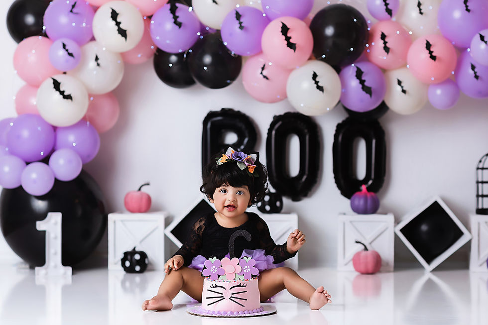 First birthday girl smashing Halloween-themed cake in purple, black, pink, and white colors during studio photo shoot.