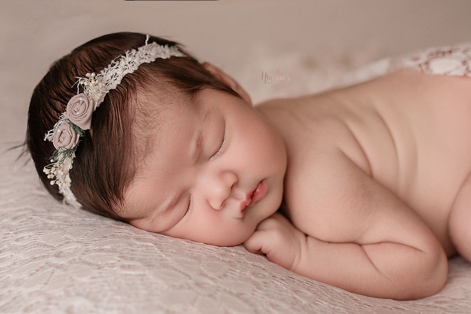 Sleeping baby with a floral headband on a lace blanket, peaceful mood, soft lighting, light pink and cream tones.