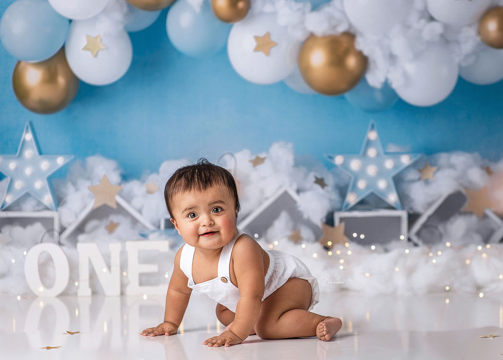One-year-old boy in blue and gold cake smash with star decorations and balloon garland