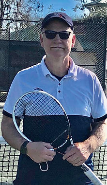 Man holding a tennis racket wearing sunglasses, cap, and collared shirt.