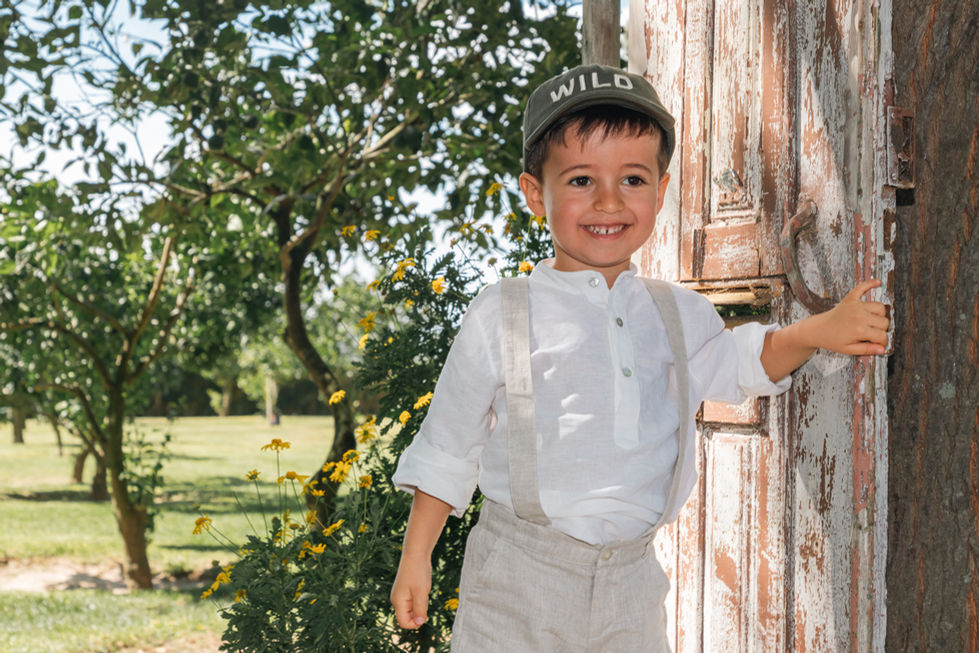 Menino sorrindo, abrindo portas na quinta do batizado. Expressão encantadora e convite caloroso aos convidados. #Batizado #AnfitriãoSorridente #MomentosEspeciais"