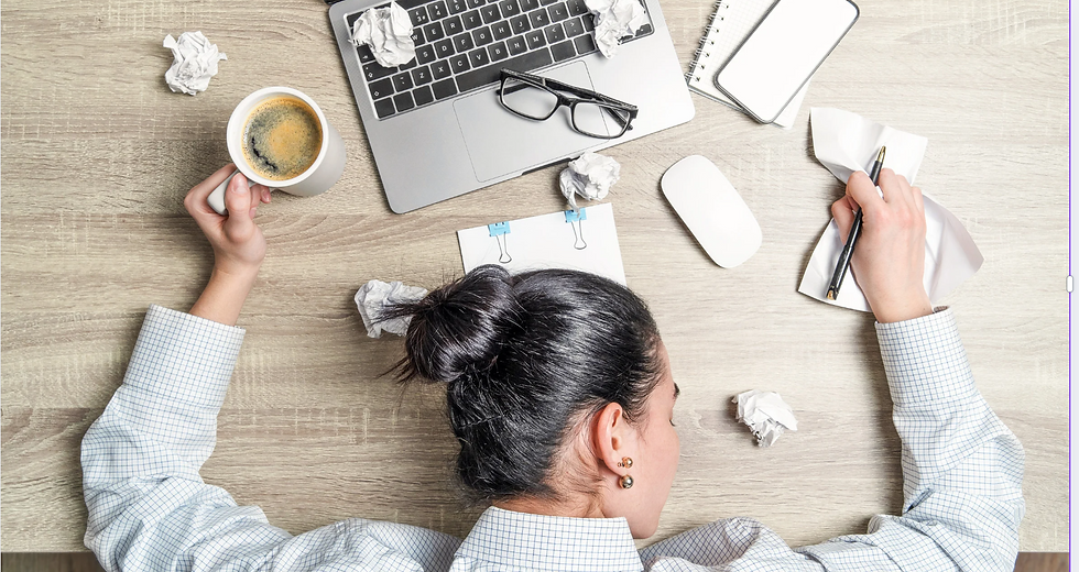 A woman lying on her laptop desk with her hand on her coffee mug and with crumbled paper all over