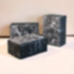 Three black soaps with intricate white swirls, staged against a light pink backdrop.