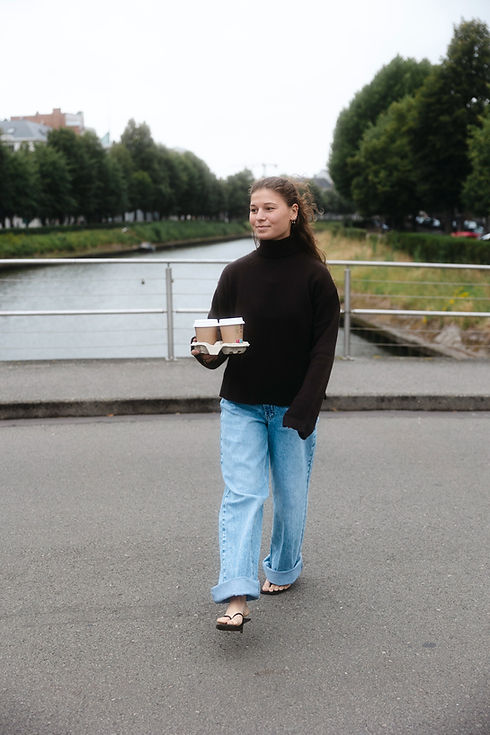 Vrouw loopt langs kanaal met koffie, casual look