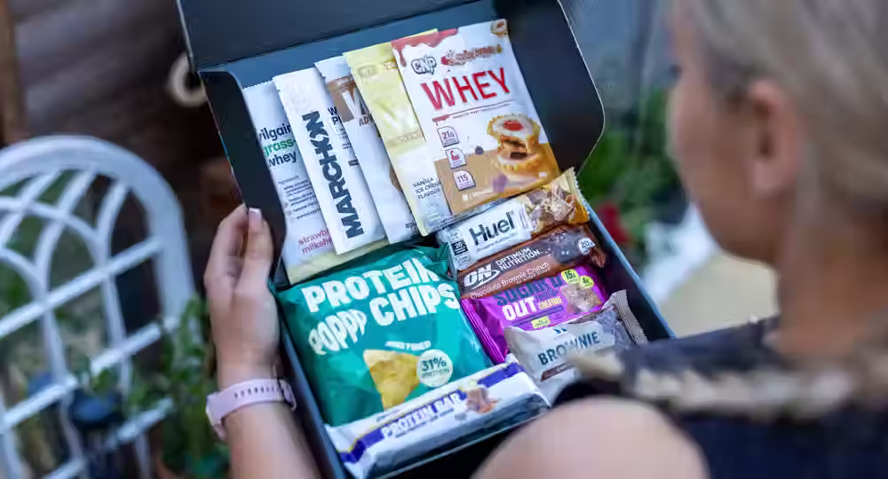 Wide-angle view of an cardboard box filled with protein snacks in a woman's arms