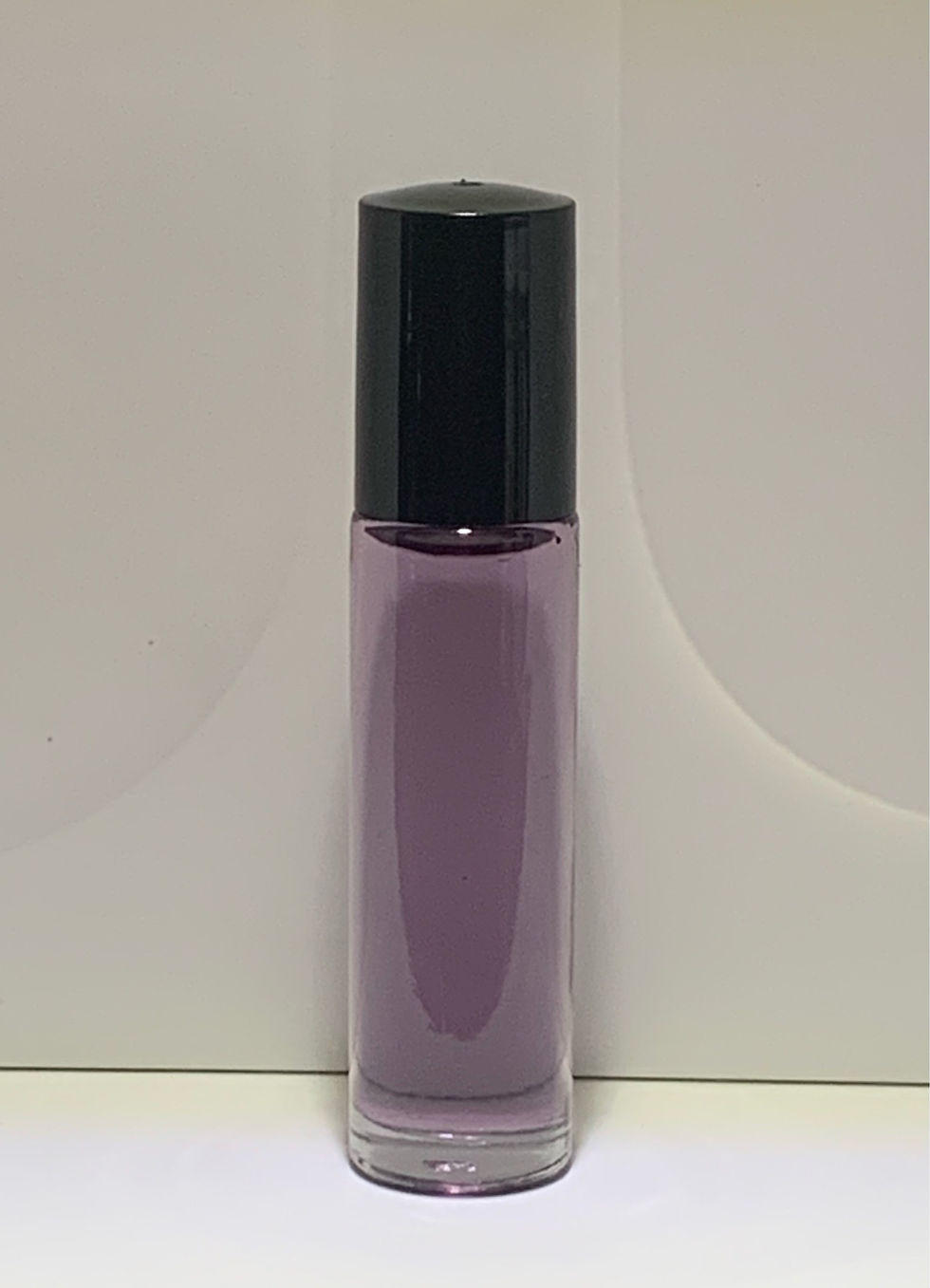 Clear glass roll-on bottle filled with purple perfume oil, topped with a black cap
