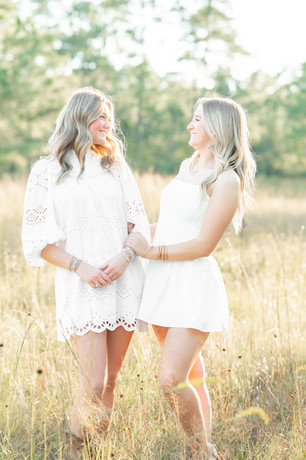 High school senior girls smiling during a senior portrait session in a yellow flower field, captured in natural light.