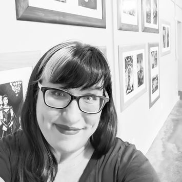 Amy is standing in front of her art at Muse Comics where she was the featured artist.