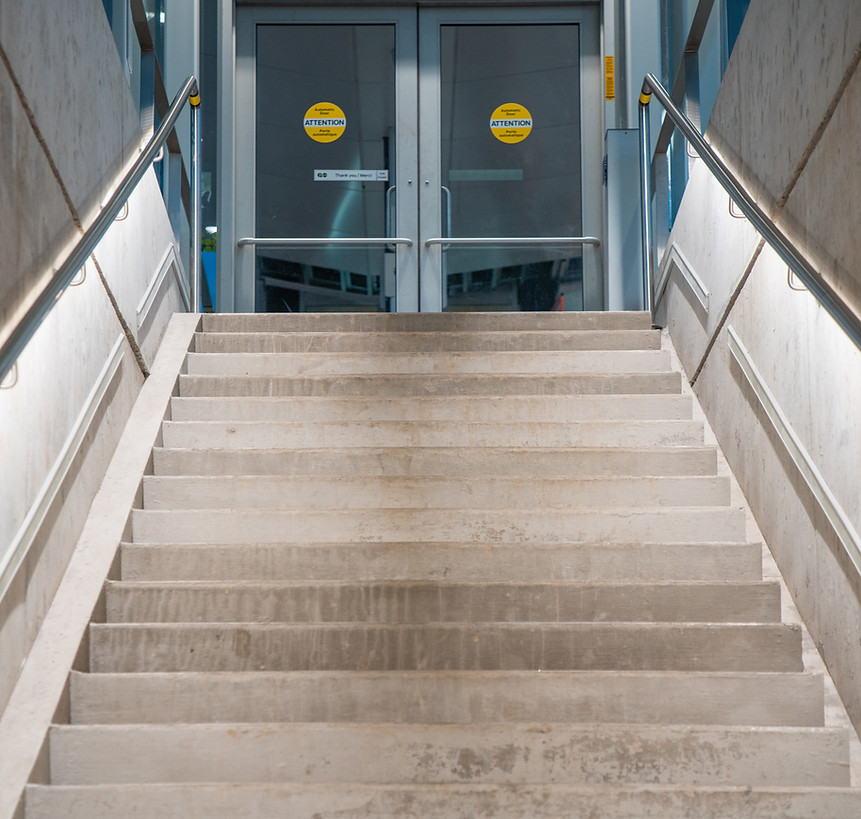 Stainless steel LED handrails illuminating a concrete staircase at a public transit entrance with automatic doors.