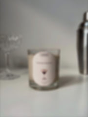 espresso martini candle showing transparent jar and dark beige, espresso inspired wax and an espresso martini on the label, decorated with a class and cocktail mixer in the background