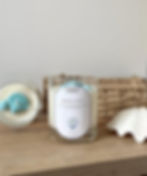 seashell coast candle showcasing two of the same candle, one upright showing the clear jar, white soy wax and label with a light blue seashell on, with the top of the candle slightly showing blue decoration. The oher candle is laid down to show the top angle of the candle with blue wax seashells 