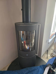 Modern sleek black cylindrical log burning stove installed against a white wall