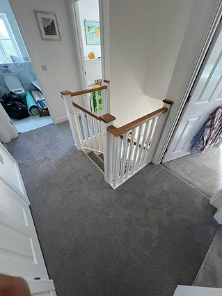 Hallway and landing area fitted with fresh grey textured carpeting around a banister