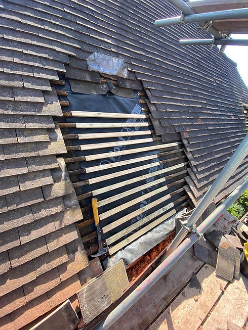 A section of a tiled roof opened up for repair, showing a black protective underlay patch and freshly installed wooden battens.