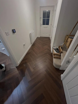 A narrow hallway with herringbone-patterned dark wood flooring