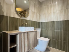 Modern toilet and wooden vanity unit with white basin in a tiled bathroom