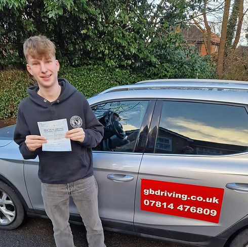 Young male student holding up his driving test certificate next to a silver tuition car