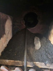 A dark interior view looking up a chimney flue filled with soot accumulation and a bird's feather.