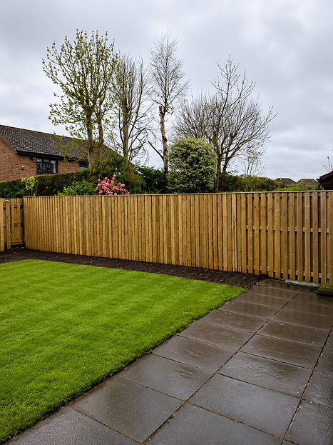 Tall wooden lap panel fence standing along neatly edged garden lawn