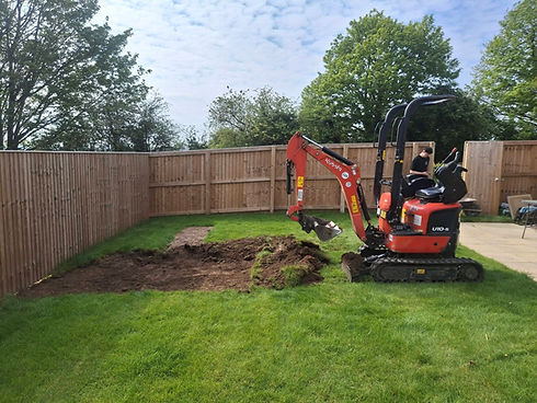 Red mini excavator machine excavating a lawn in a garden enclosed by wooden fencing