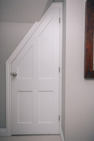 Custom white under-stairs storage cupboard door fitted to a wall
